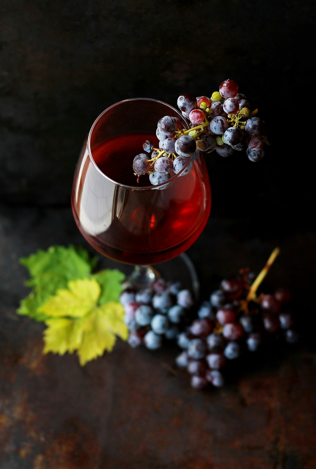 Red wine glass with grapes on dark moody background