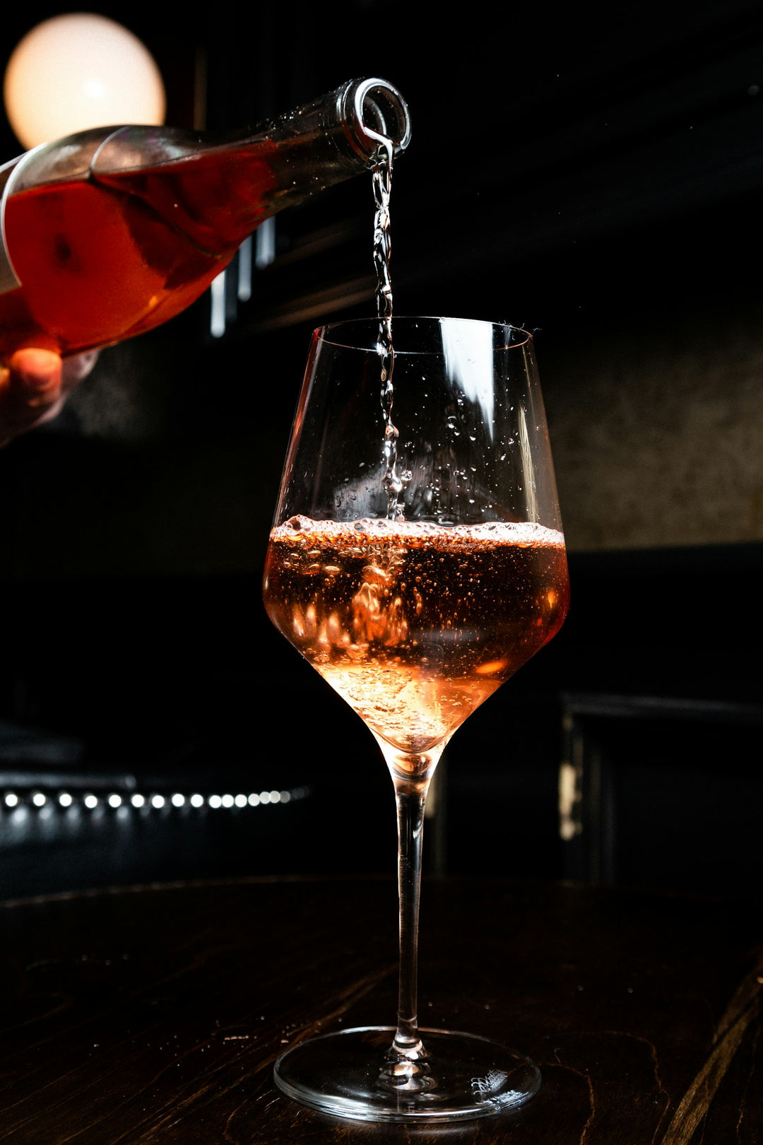 Rosé being poured into a wine glass at a dim bar